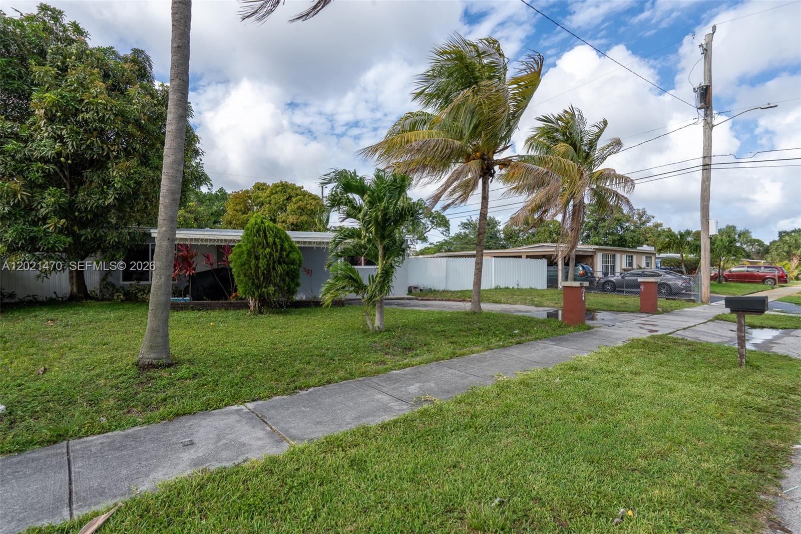 A single-story house with a lawn, palm trees, and a driveway under a cloudy sky — 3235 NW 2nd St, Lauderhill FL 33311, LAUDERHILL, FL