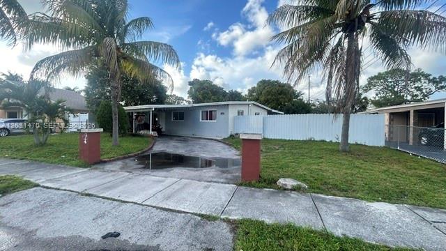 A single-story house with a driveway and palm trees sits behind a white fence — 3235 NW 2nd St, Lauderhill FL 33311, LAUDERHILL, FL