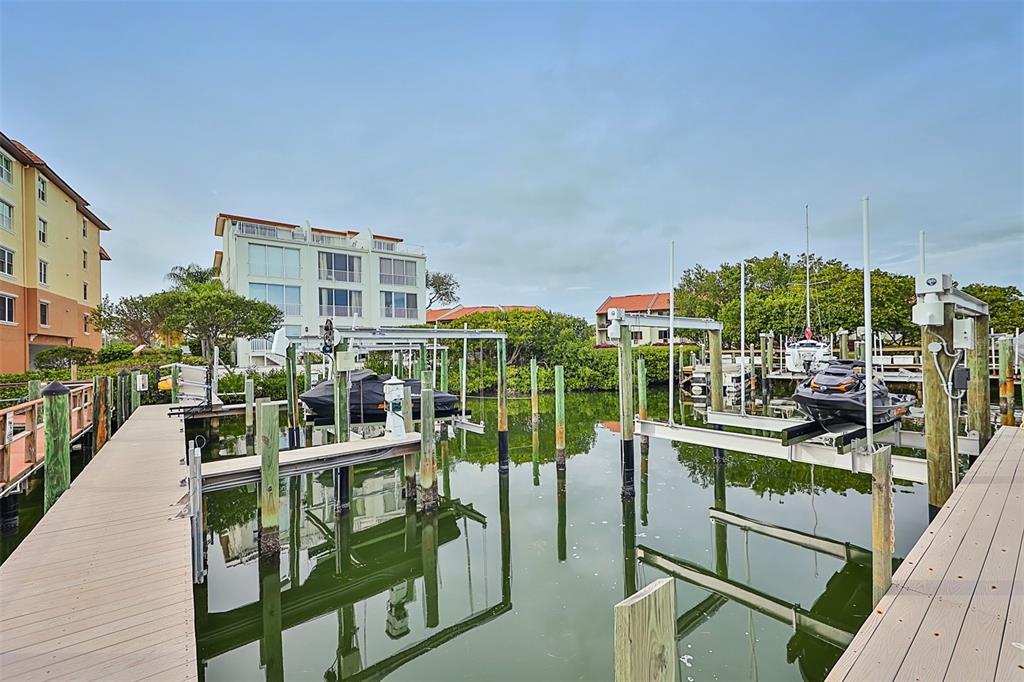A wooden dock leads to boat lifts holding a covered boat and a jet ski — 1593 PINELLAS BAYWAY S, TIERRA VERDE, FL