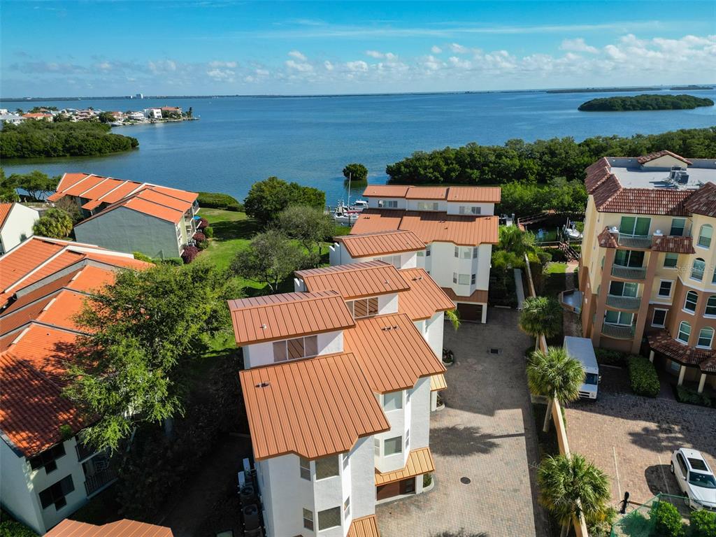 An aerial view shows multi-story residential buildings with metal roofs near a large body of water — 1593 PINELLAS BAYWAY S, TIERRA VERDE, FL