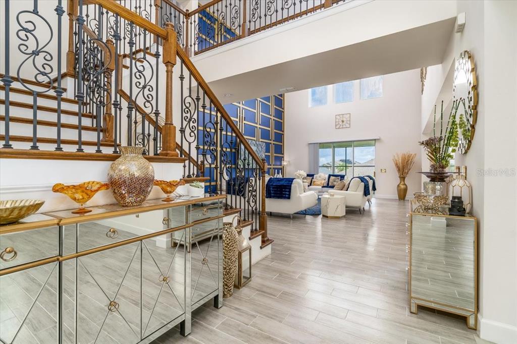 A grand foyer features a mirrored console table, a staircase with iron railings, and tile flooring — 1296 WATERVIEW RIDGE CIRCLE, APOPKA, FL