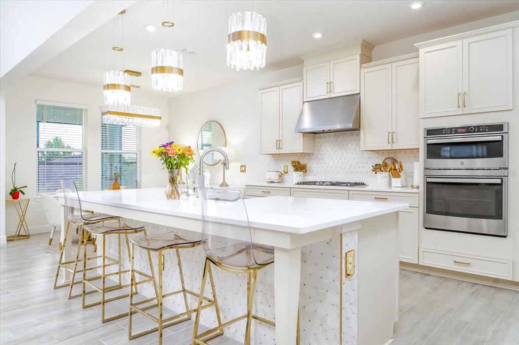 A bright kitchen features a large white island, gold-accented bar stools, and stainless steel appliances — 1296 WATERVIEW RIDGE CIRCLE, APOPKA, FL