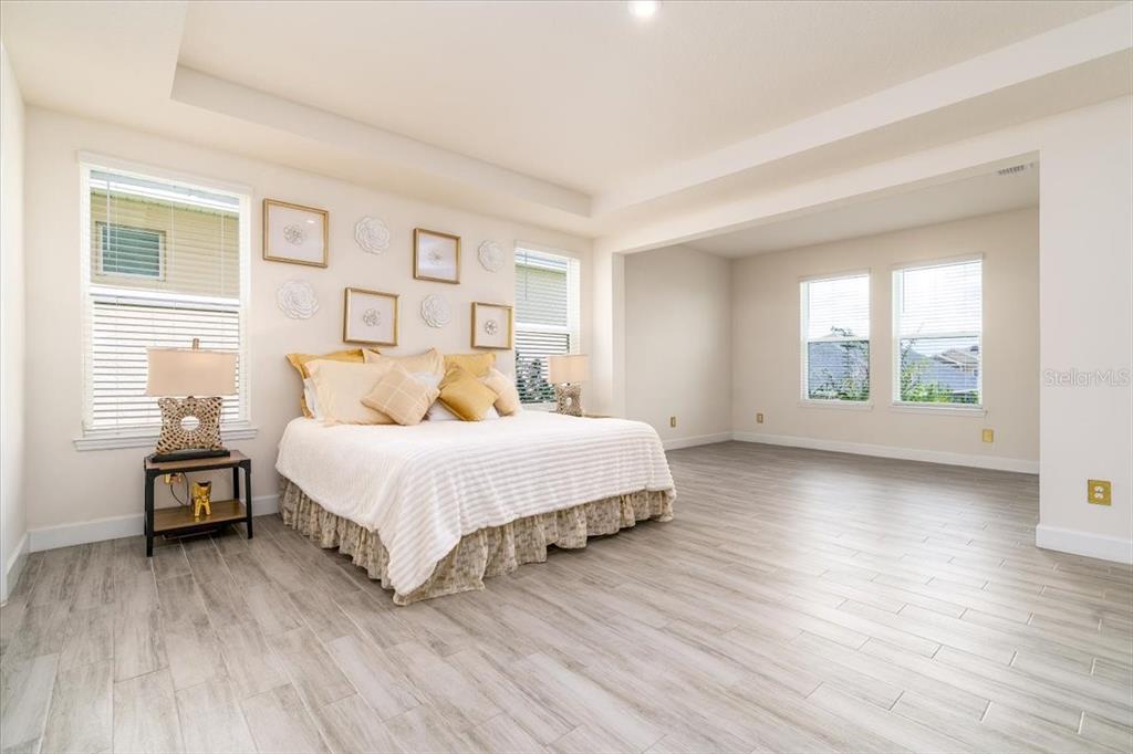 A spacious bedroom features light wood-look tile flooring, a tray ceiling, and a king-sized bed — 1296 WATERVIEW RIDGE CIRCLE, APOPKA, FL