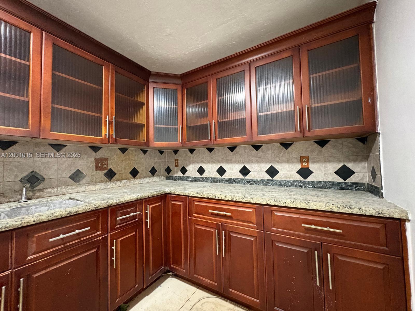 A kitchen features cherry wood cabinets, glass-paneled upper doors, and speckled granite countertops — 2531 NW 88th St # 2531, Miami FL 33147, MIAMI, FL