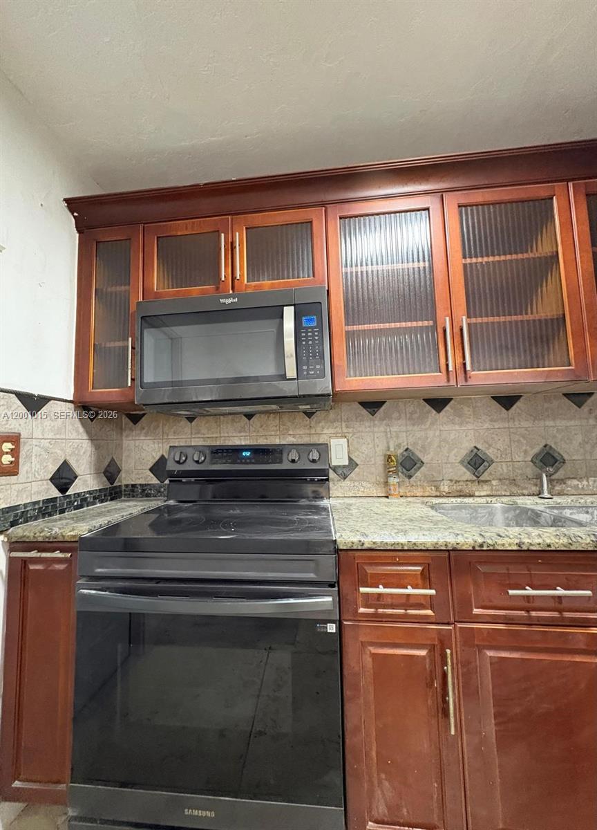 A kitchen features dark wood cabinets, a black stove, a microwave, and granite countertops — 2531 NW 88th St # 2531, Miami FL 33147, MIAMI, FL
