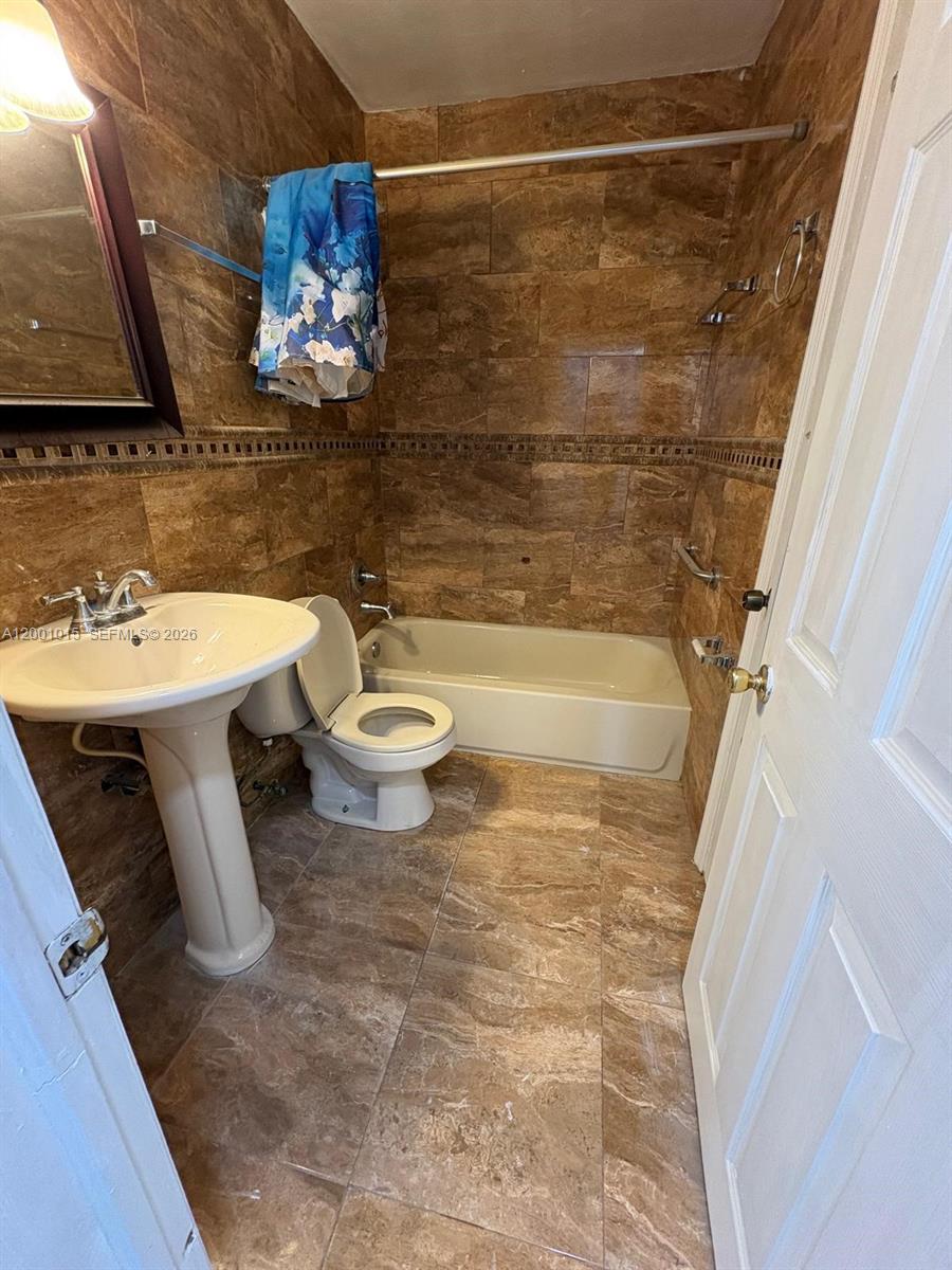 A bathroom features brown tiled walls and floors, a pedestal sink, and a bathtub — 2531 NW 88th St # 2531, Miami FL 33147, MIAMI, FL