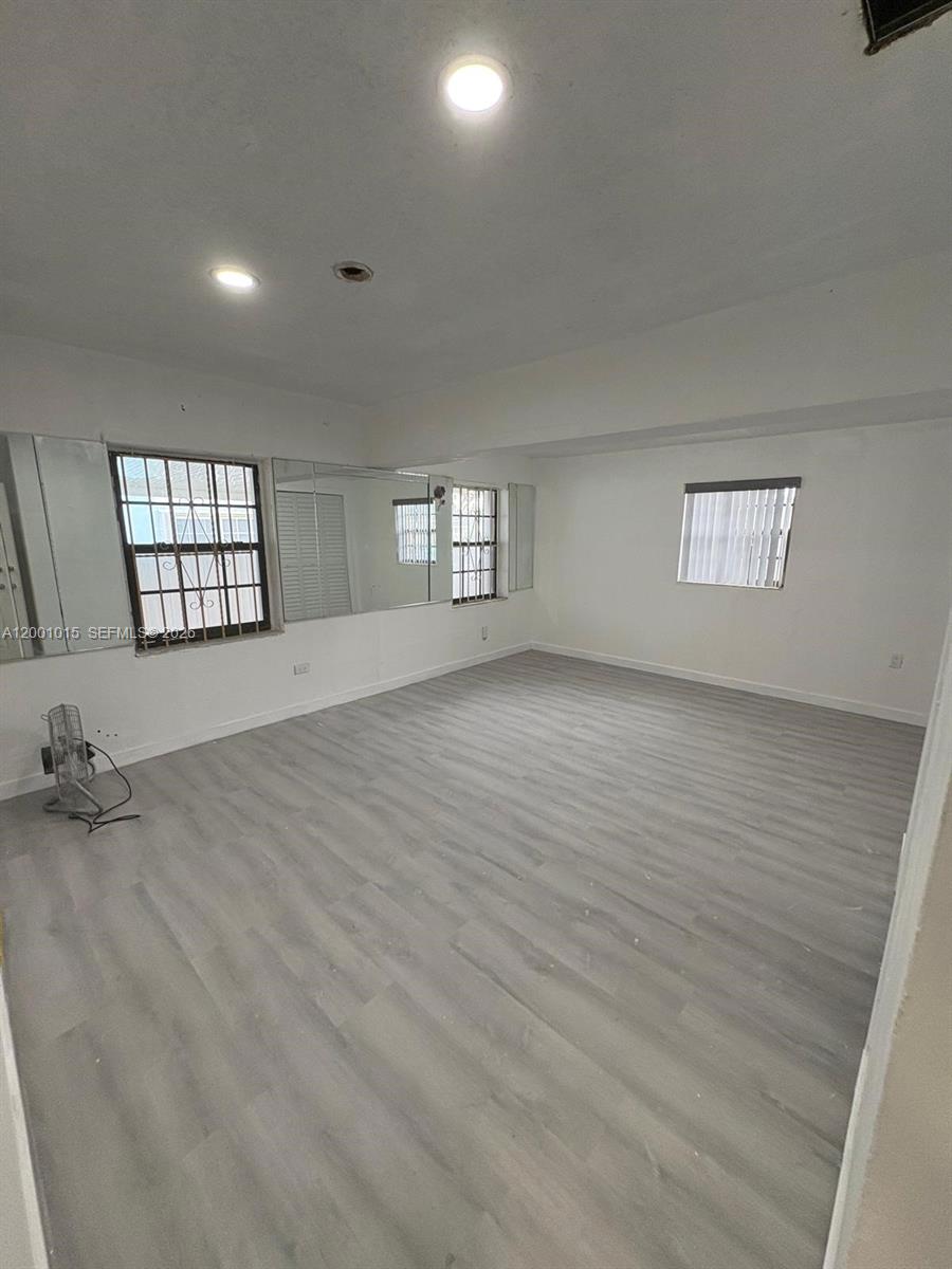 An empty room features light gray wood-look flooring, white walls, recessed lighting, and mirrored accents — 2531 NW 88th St # 2531, Miami FL 33147, MIAMI, FL