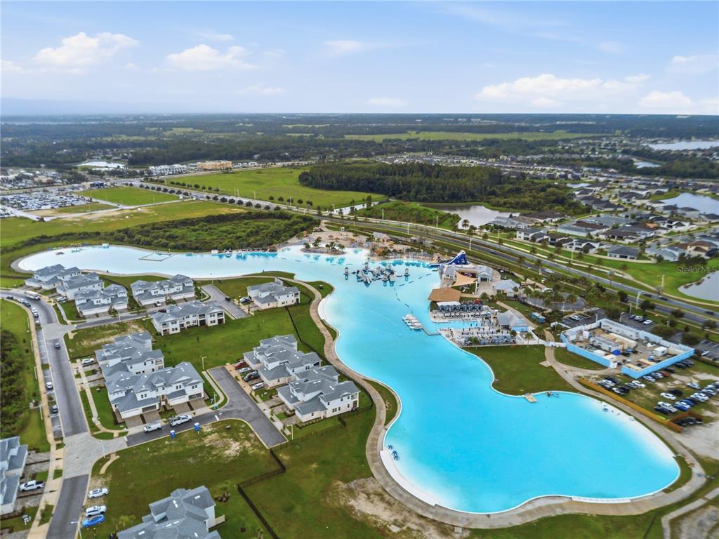 An aerial view shows a large turquoise lagoon surrounded by residential buildings and green space — 31730 SUN KETTLE LOOP, WESLEY CHAPEL, FL
