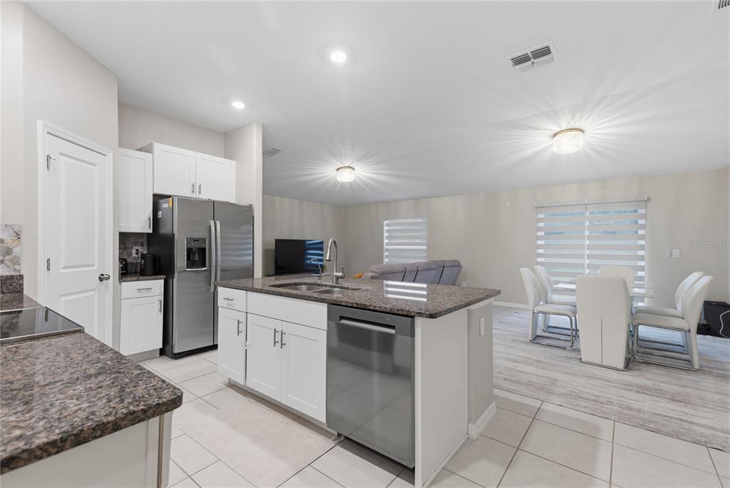 A kitchen with white cabinets, granite countertops, and stainless steel appliances opens to a dining area — 31730 SUN KETTLE LOOP, WESLEY CHAPEL, FL