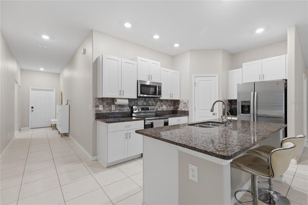 A kitchen features white cabinets, granite countertops, a center island with bar stools, and tile flooring — 31730 SUN KETTLE LOOP, WESLEY CHAPEL, FL