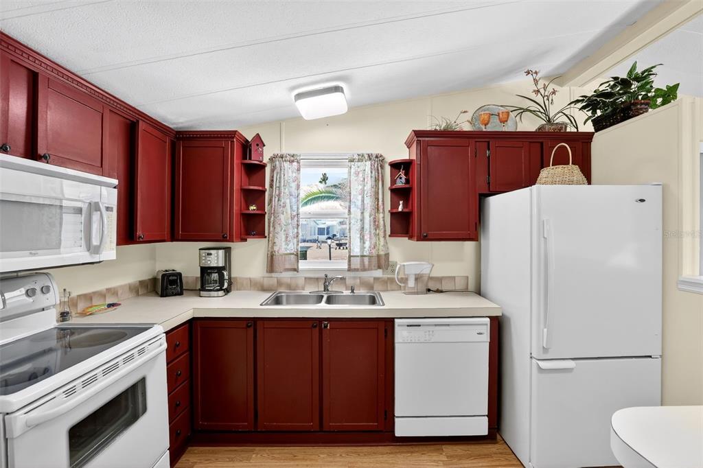 A kitchen features red cabinets, white appliances, a double sink, and a window with curtains — 855 IGLESIA DRIVE, NORTH PORT, FL