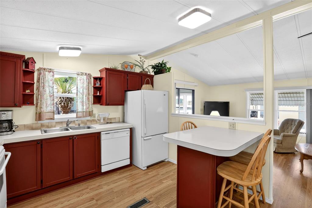 A kitchen with red cabinets, white appliances, and a breakfast bar overlooking a living area — 855 IGLESIA DRIVE, NORTH PORT, FL