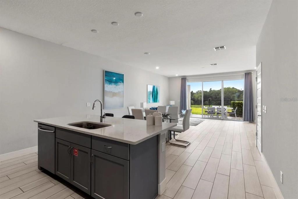 A kitchen island with a sink overlooks an open dining area and a glass sliding door — 832 DRIVING RANGE COURT, KISSIMMEE, FL