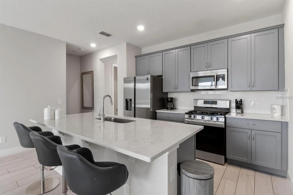 A modern kitchen features gray cabinets, stainless steel appliances, and a large quartz-topped island — 832 DRIVING RANGE COURT, KISSIMMEE, FL