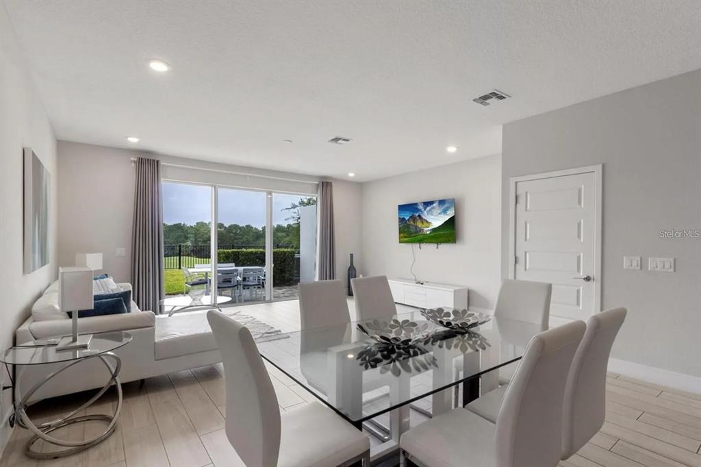 A bright, open-concept living and dining area features white tile floors, modern furniture, and sliding doors — 832 DRIVING RANGE COURT, KISSIMMEE, FL