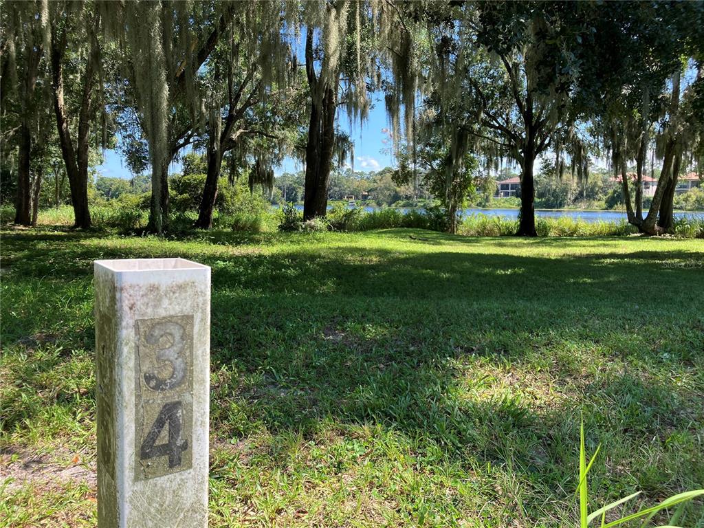 A grassy lot with a numbered post in the foreground overlooks a lake and trees — 3613 AZURITE COURT, DELAND, FL