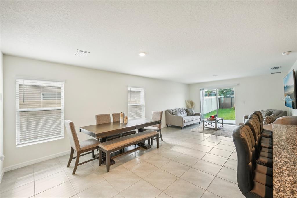 An open-concept living and dining area features tile flooring, neutral walls, and a sliding glass door — 11637 SAW PALMETTO LANE, RIVERVIEW, FL