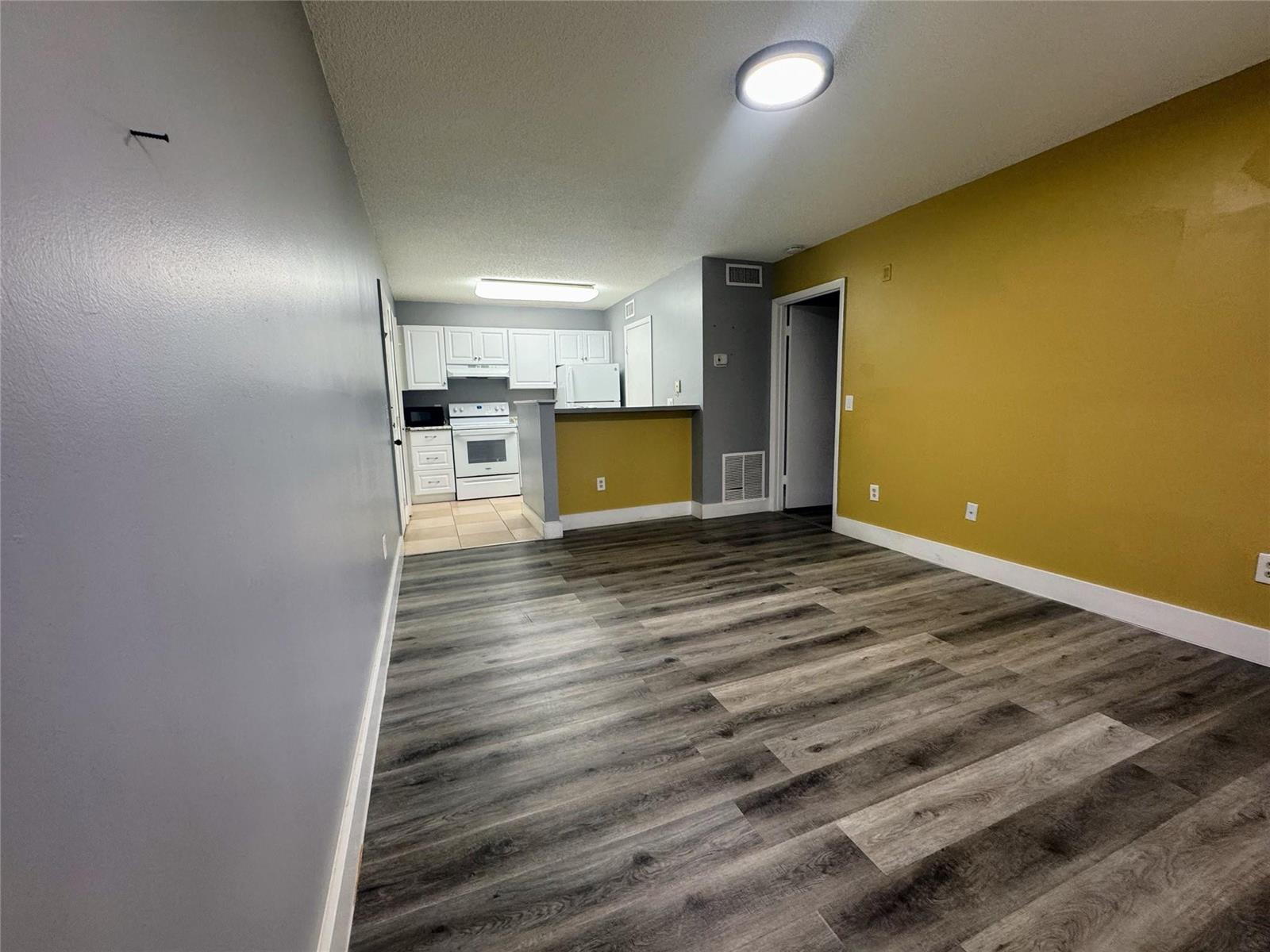 An open-concept living area with gray walls, a yellow accent wall, and wood-look flooring — 4361 W Mcnab Road # 17, Pompano Beach FL 33069, POMPANO BEACH, FL
