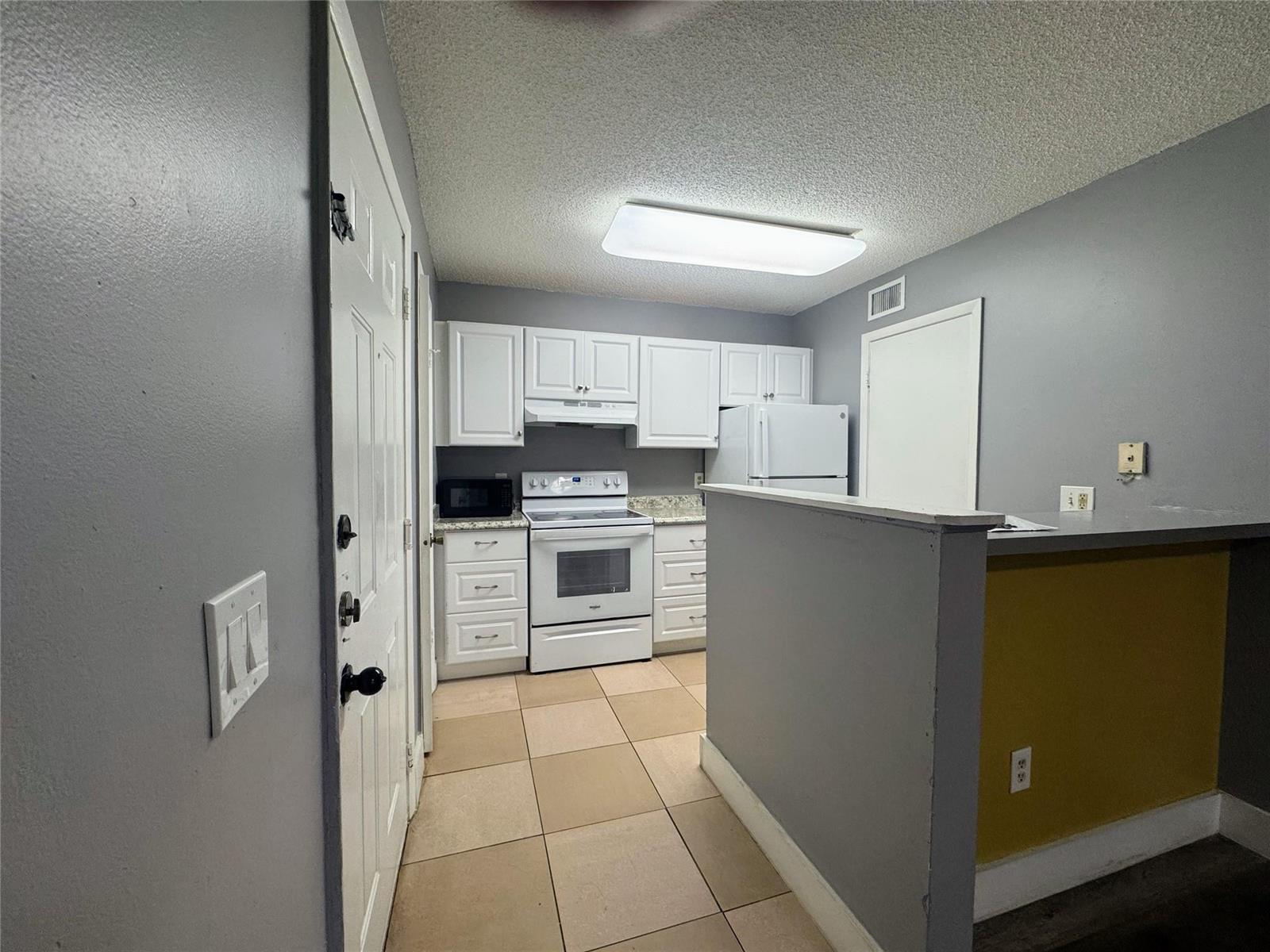 A kitchen features white cabinets, white appliances, gray walls, and light-colored floor tiles — 4361 W Mcnab Road # 17, Pompano Beach FL 33069, POMPANO BEACH, FL