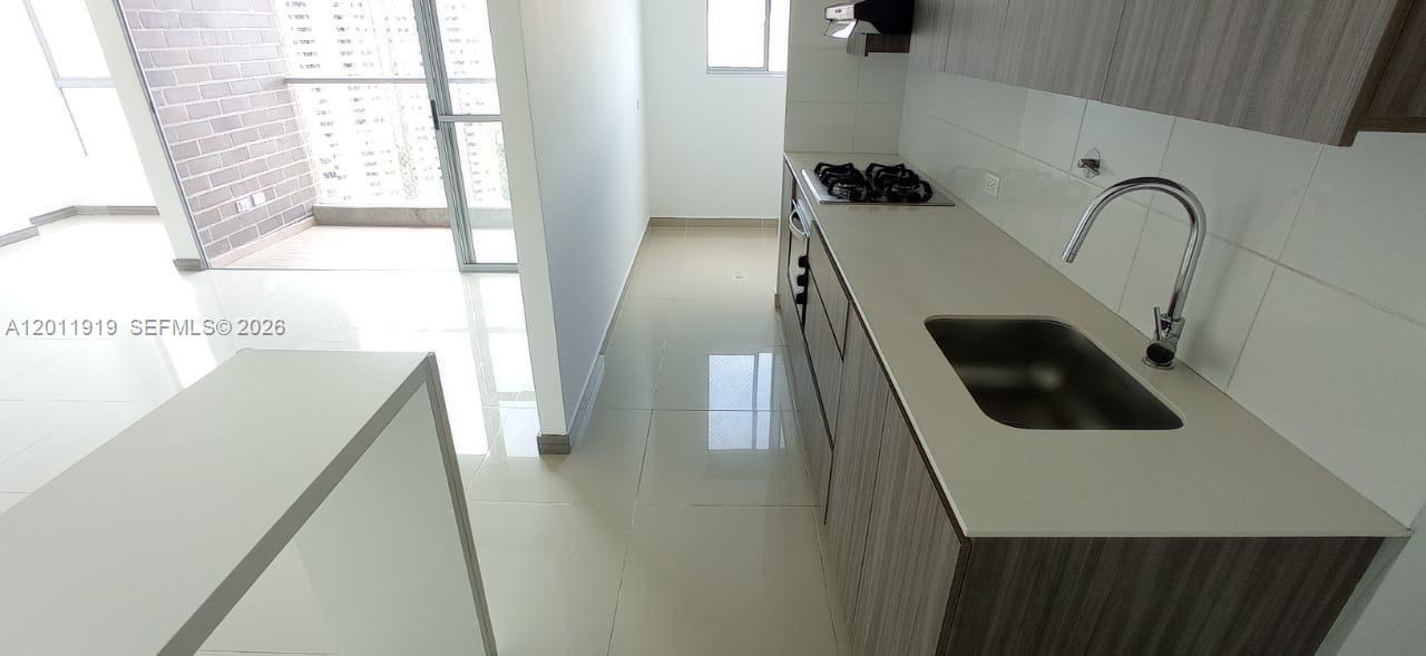 A modern kitchen features light-colored countertops, wood-toned cabinets, and a view of a balcony — 53-90 Calle 75 AA Sur # 2601, FL 055413, FL