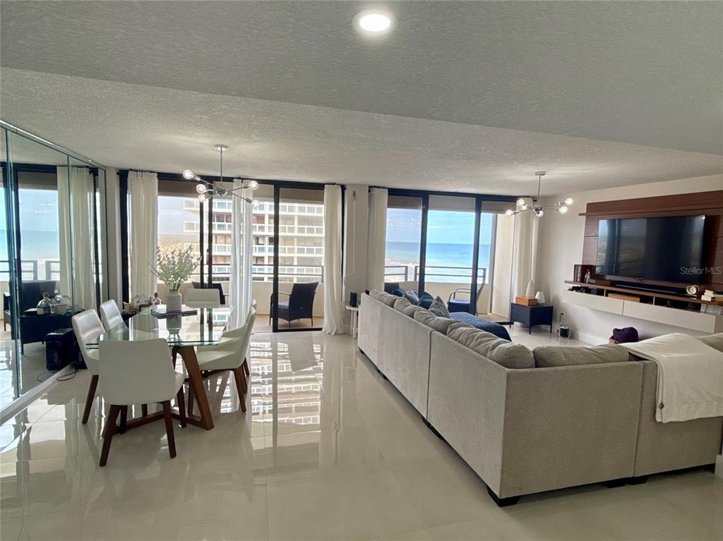An open-concept living and dining area features white tile floors, a sectional sofa, and balconies — 2900 N ATLANTIC AVENUE UNIT 1503, DAYTONA BEACH, FL
