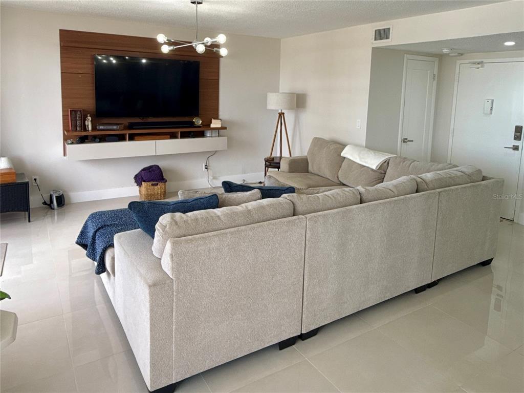 A living room features a large sectional sofa, a wall-mounted television, and light-colored tile flooring — 2900 N ATLANTIC AVENUE UNIT 1503, DAYTONA BEACH, FL