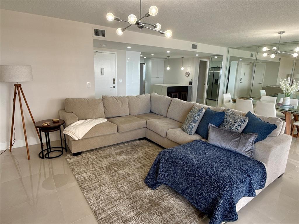 A living room features a large beige sectional sofa, a textured rug, and modern lighting — 2900 N ATLANTIC AVENUE UNIT 1503, DAYTONA BEACH, FL