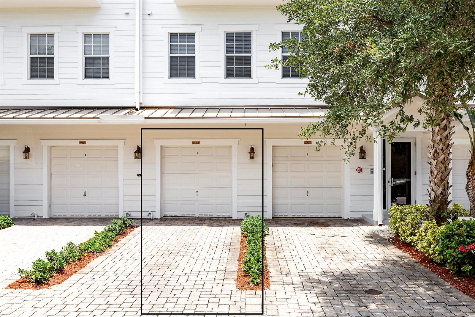 A white townhouse exterior features three garage doors, brick paver driveways, and small landscaped hedges — 6807 Lakeside Circle N # 1, Davie FL 33314, DAVIE, FL