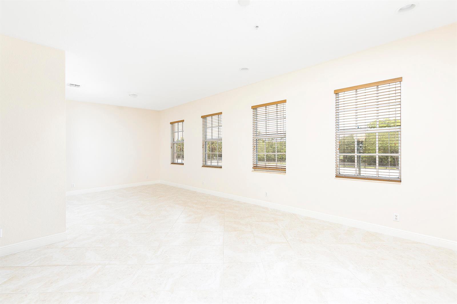 An empty room with beige tile flooring, light-colored walls, and four windows with blinds — 6807 Lakeside Circle N # 1, Davie FL 33314, DAVIE, FL