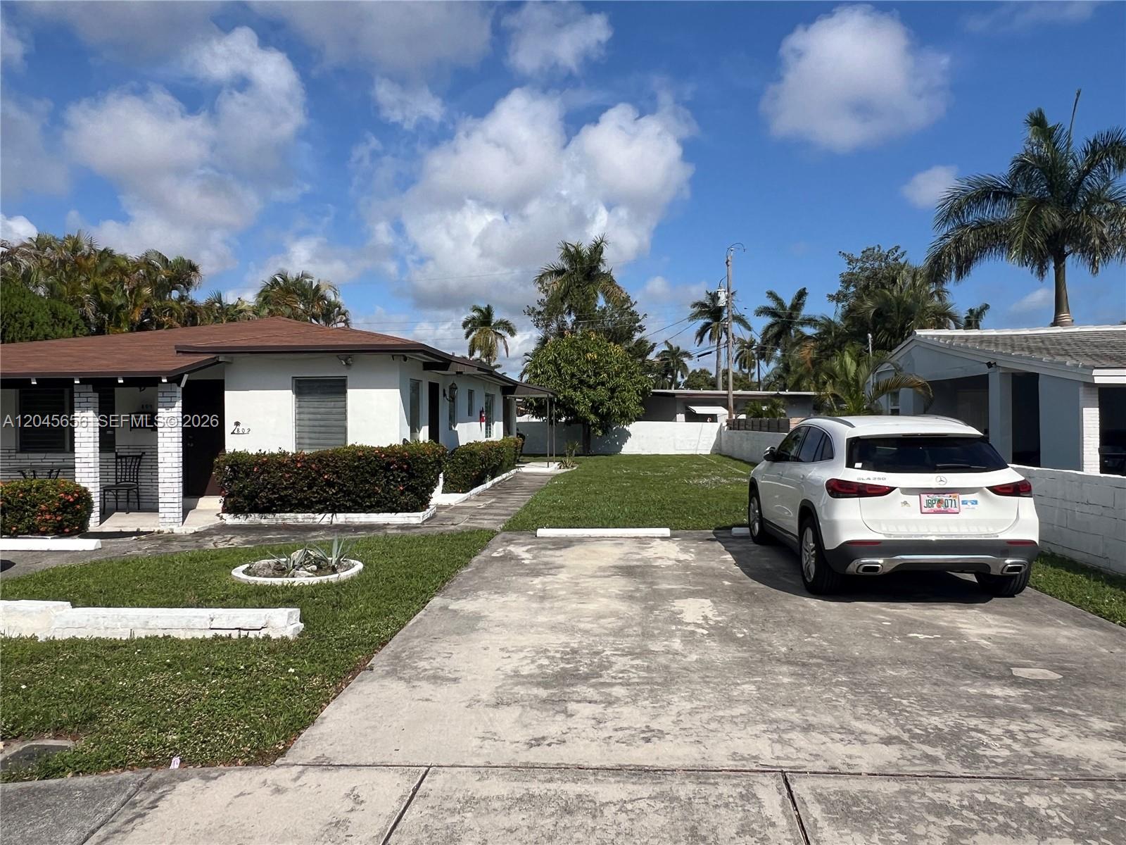 A white house with a brown roof sits next to a driveway with a parked car — 809 NE 2nd St unit 1-2, Hallandale Beach FL 33009, HALLANDALE BEACH, FL