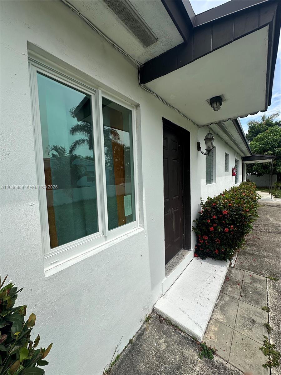 A white exterior wall features a dark brown door, a large window, and landscaping — 809 NE 2nd St unit 1-2, Hallandale Beach FL 33009, HALLANDALE BEACH, FL