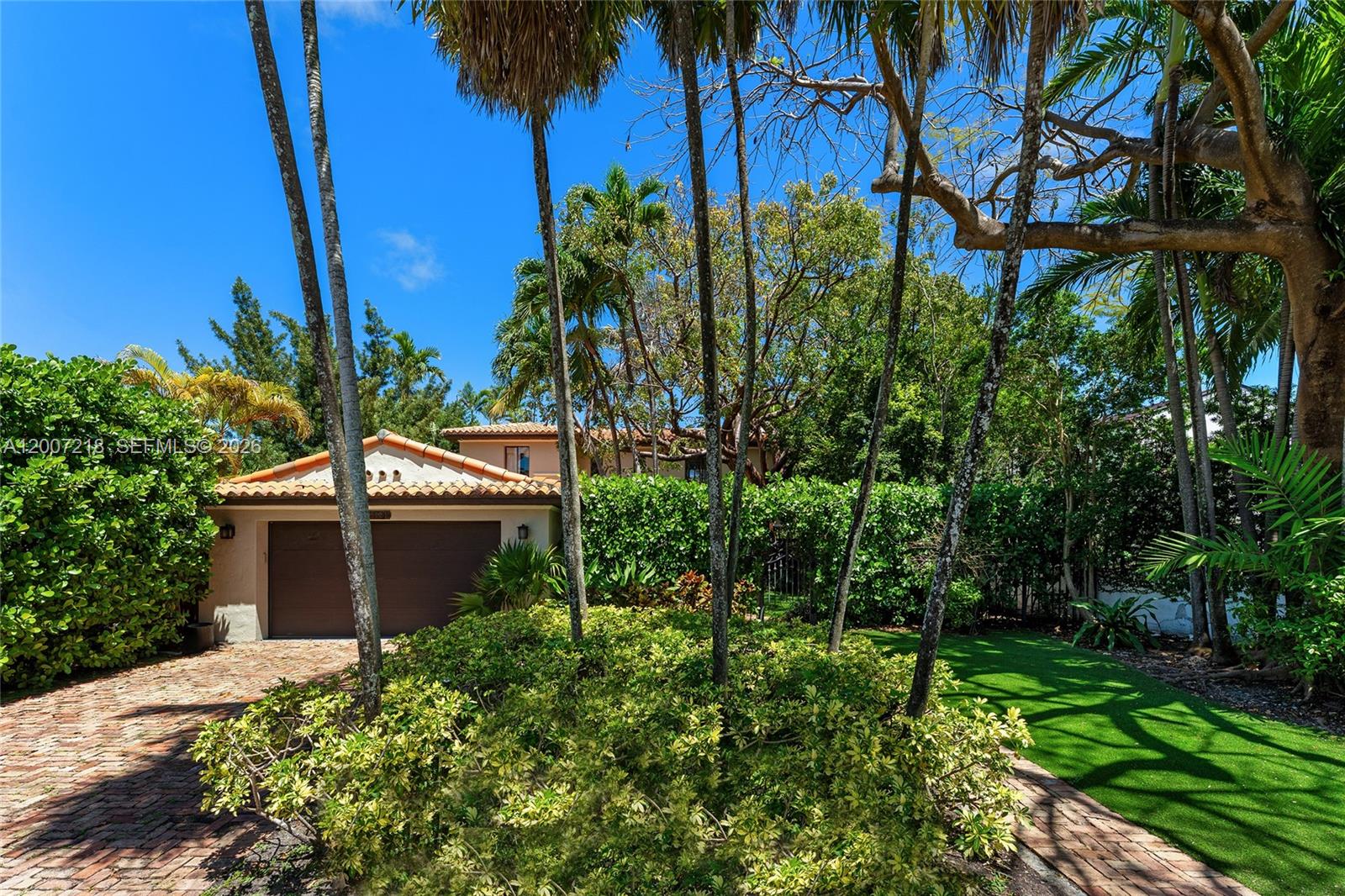 A single-story house with a brown garage door and a brick driveway surrounded by trees — 6121 La Gorce Dr, Miami Beach FL 33140, MIAMI BEACH, FL