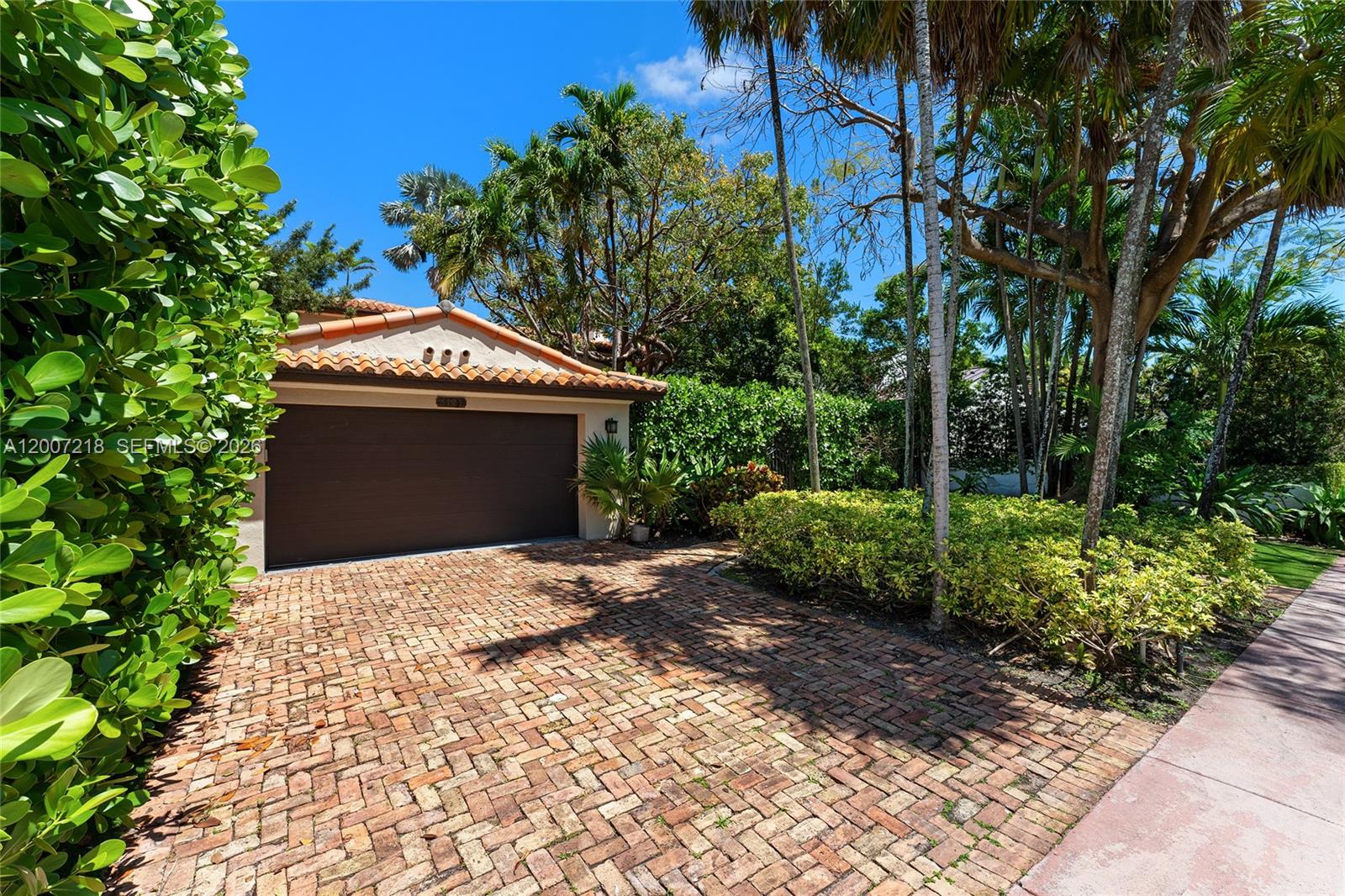 A brick driveway leads to a single-car garage with a tile roof and lush landscaping — 6121 La Gorce Dr, Miami Beach FL 33140, MIAMI BEACH, FL