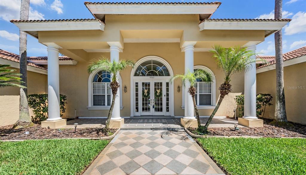 The exterior of a house features a tiled walkway leading to a columned entryway — 4561 ROANOAK WAY, PALM HARBOR, FL