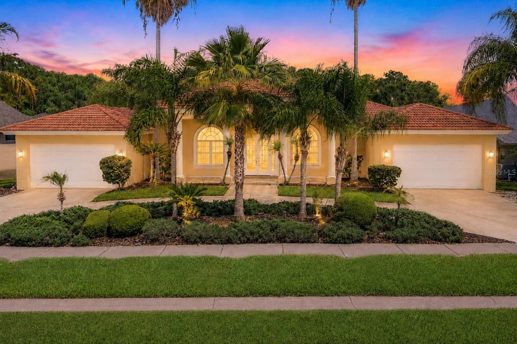 A single-story house with a tile roof, two garages, and palm trees at sunset — 4561 ROANOAK WAY, PALM HARBOR, FL
