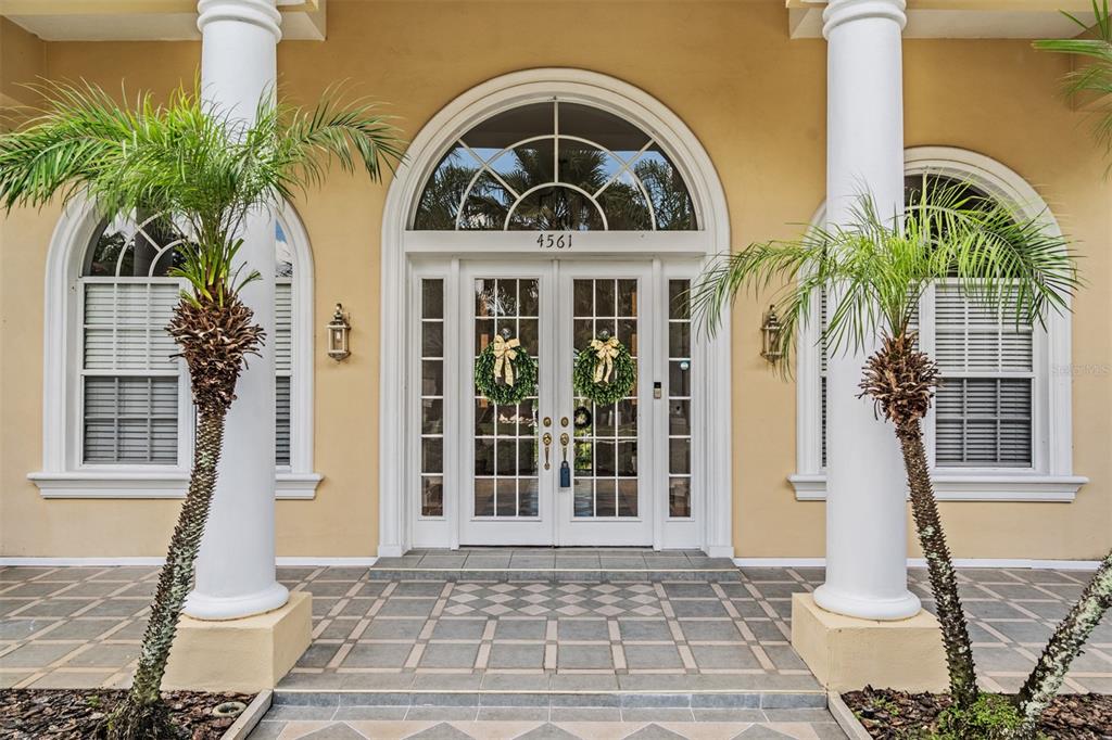 The front entrance of a house features white columns, double glass doors, and two palm trees — 4561 ROANOAK WAY, PALM HARBOR, FL