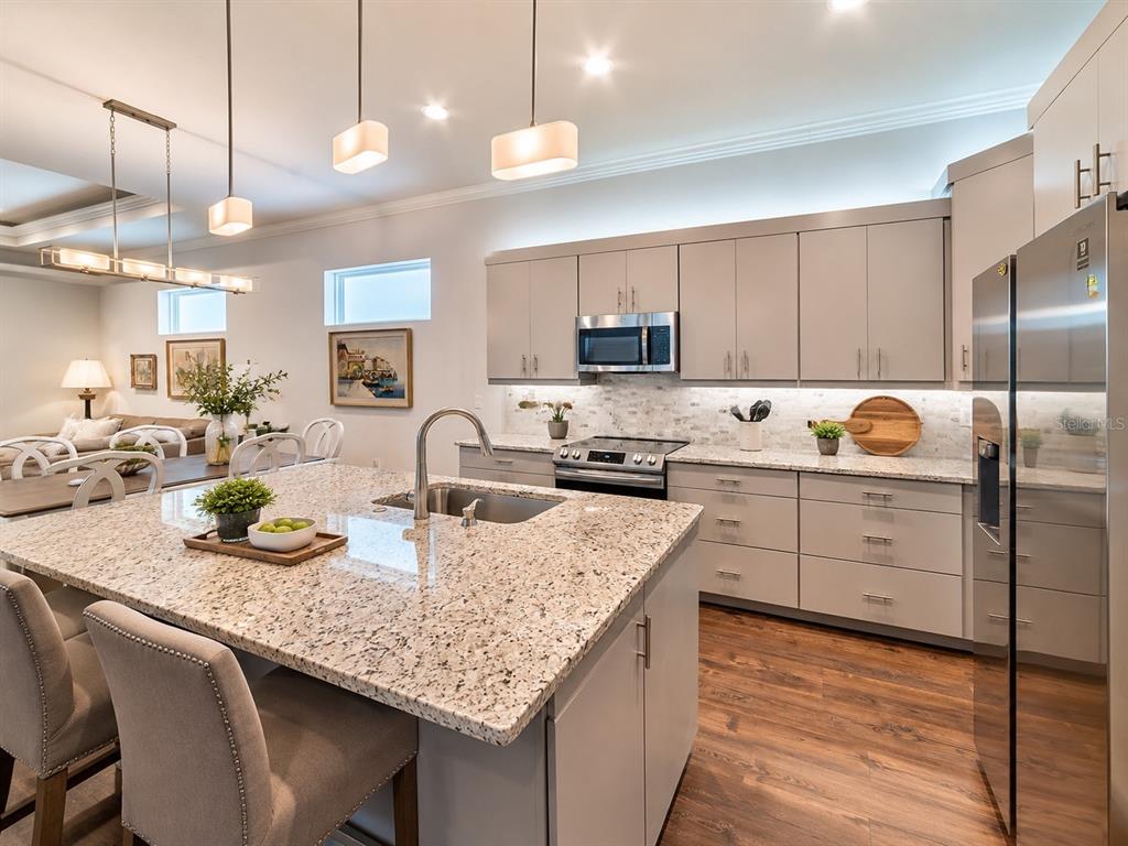 A modern kitchen features a granite-topped island, light gray cabinetry, and stainless steel appliances — 6463 SW 77TH DRIVE, GAINESVILLE, FL