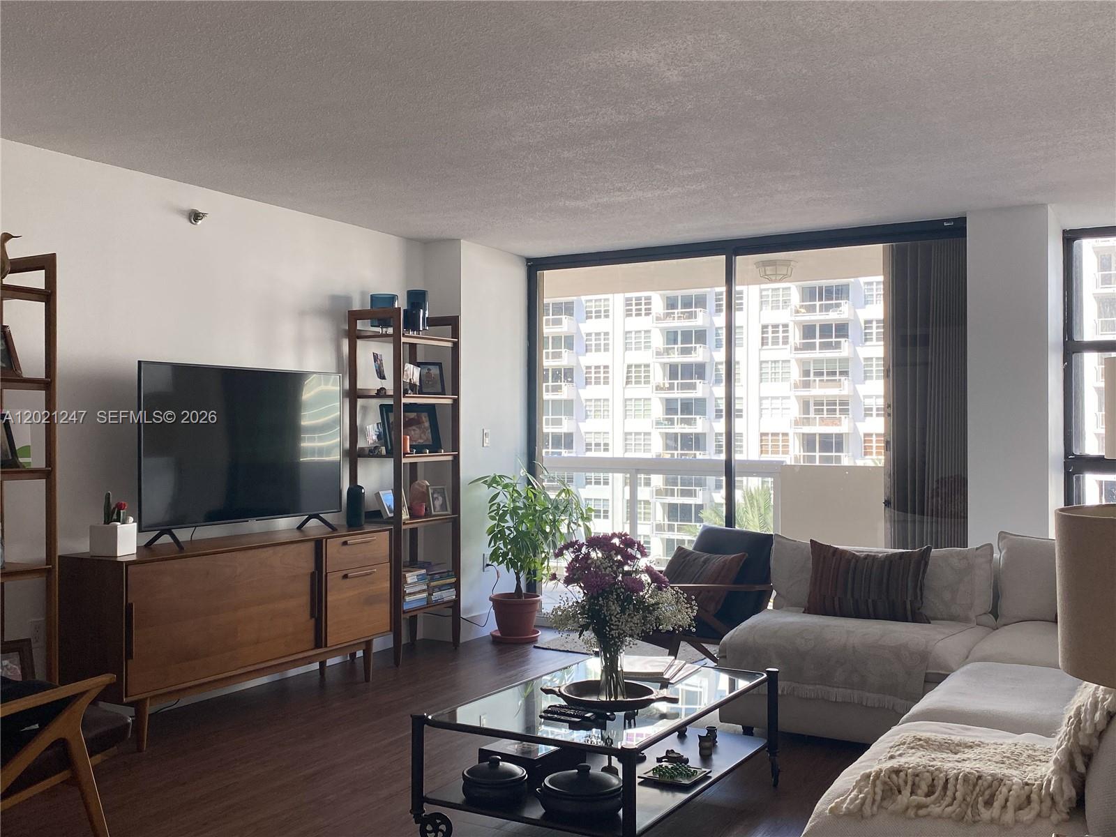 A living room features a wooden media console, a glass coffee table, and large windows — 5757 Collins Ave # 703, Miami Beach FL 33140, MIAMI BEACH, FL