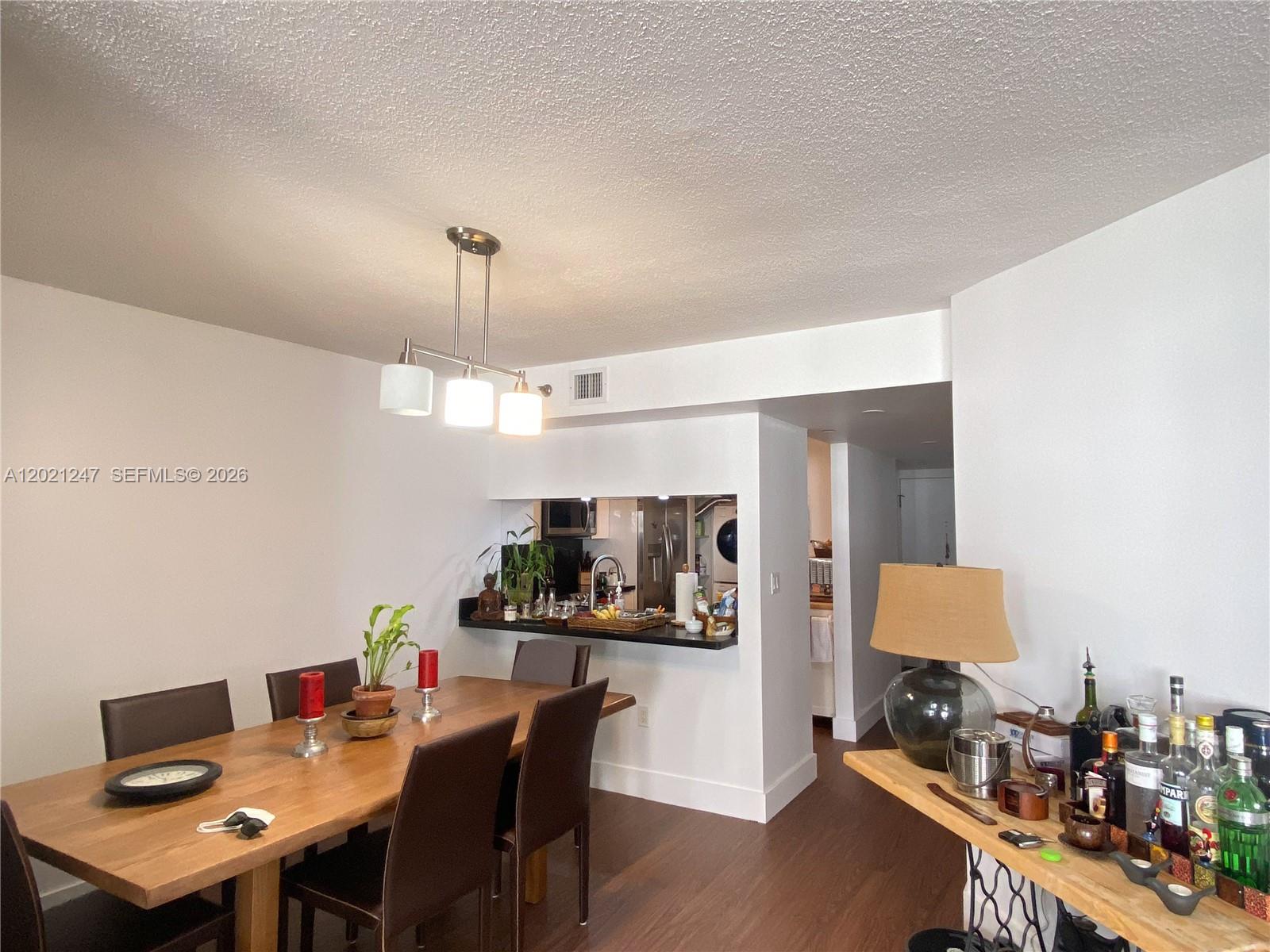 A dining room features a wooden table, dark chairs, a pendant light, and an open kitchen — 5757 Collins Ave # 703, Miami Beach FL 33140, MIAMI BEACH, FL