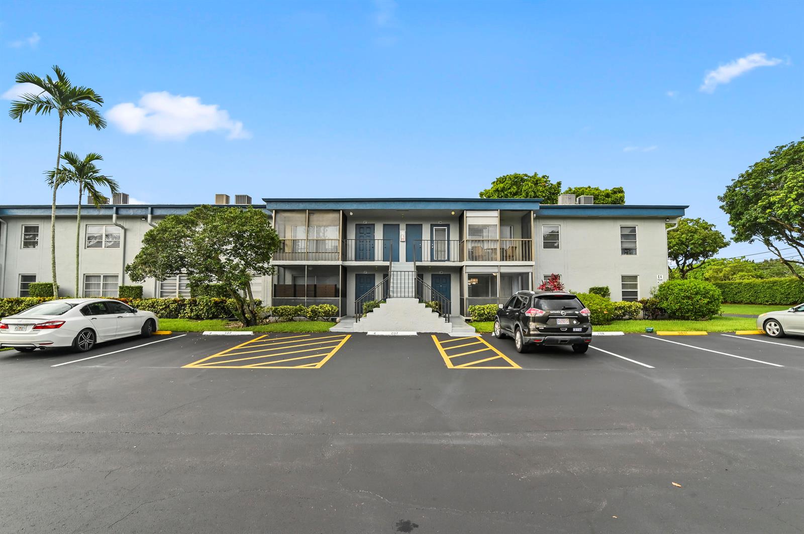 A two-story apartment building with a central staircase and parking lot in the foreground — 7535 S Oriole Boulevard # 108, Delray Beach FL 33446, DELRAY BEACH, FL