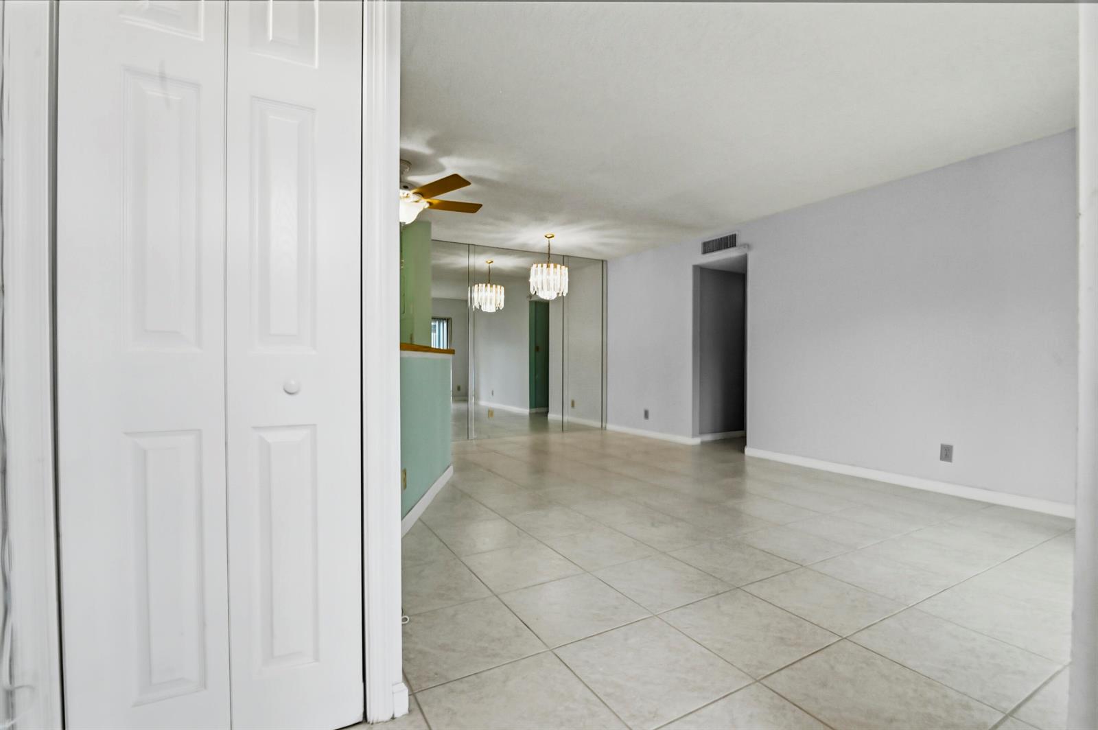 An interior view of a room with light-colored tile flooring, mirrored walls, and a chandelier — 7535 S Oriole Boulevard # 108, Delray Beach FL 33446, DELRAY BEACH, FL
