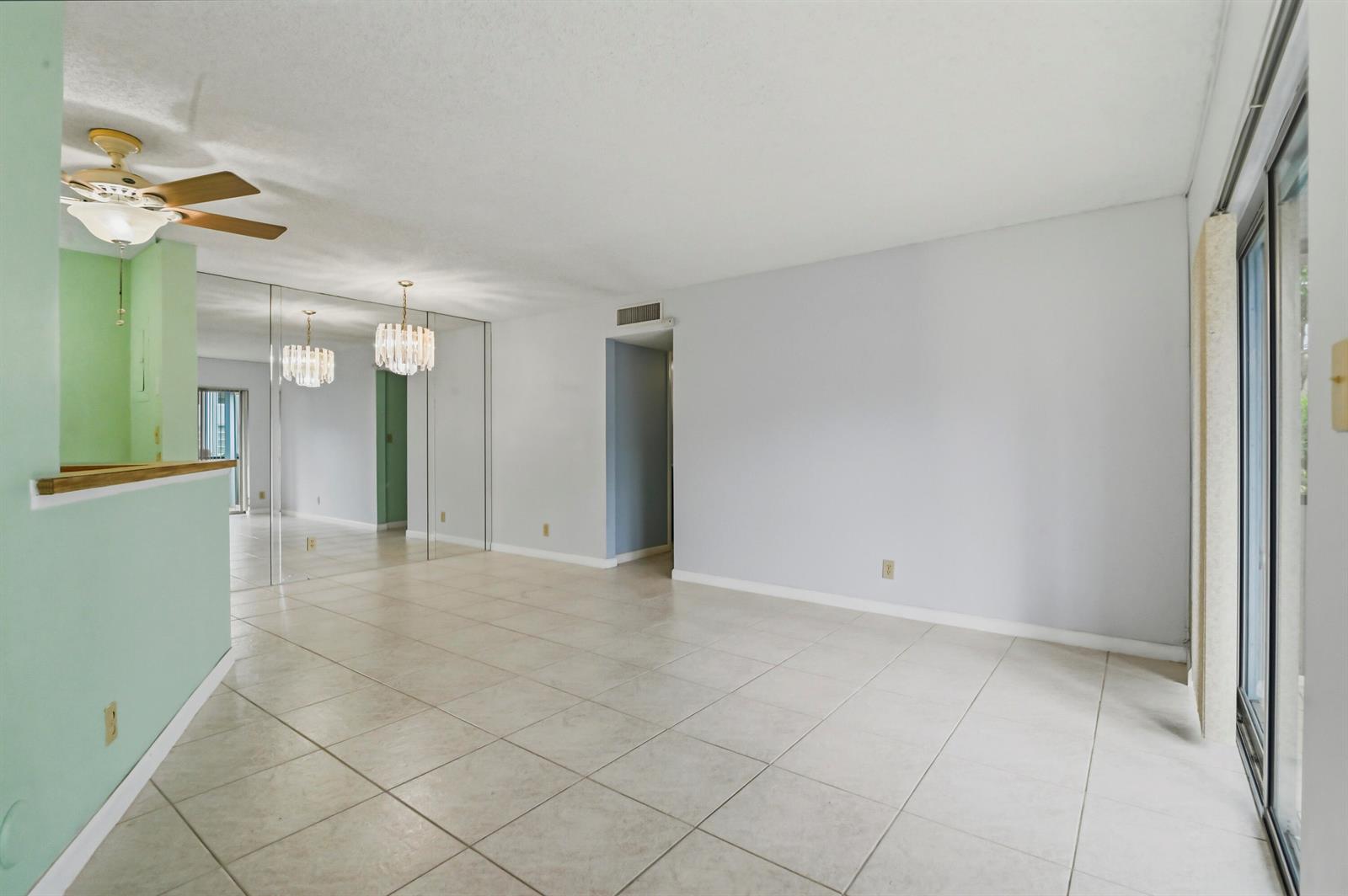 An empty living room with light-colored tile flooring, mirrored walls, and a ceiling fan — 7535 S Oriole Boulevard # 108, Delray Beach FL 33446, DELRAY BEACH, FL