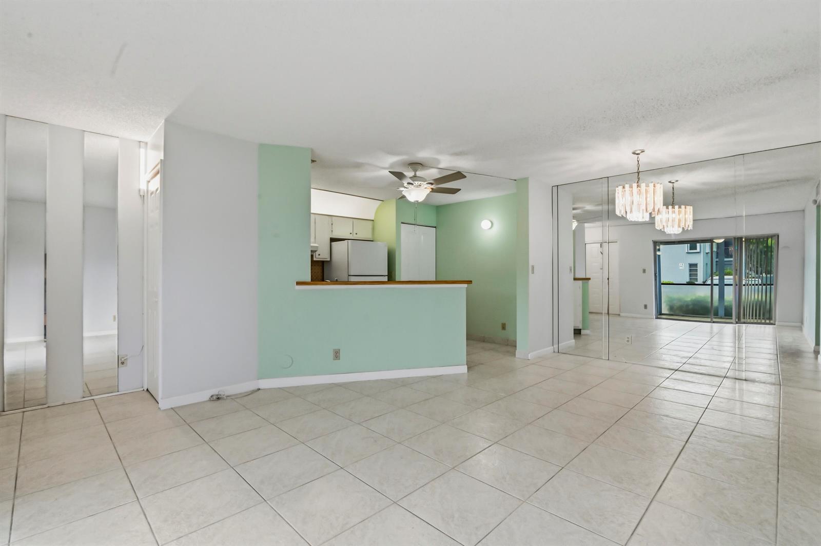 An open-concept living and dining area features light green walls, tile flooring, and mirrored walls — 7535 S Oriole Boulevard # 108, Delray Beach FL 33446, DELRAY BEACH, FL