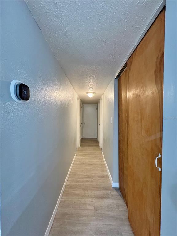 A hallway features light wood-look flooring, light blue walls, and a wooden sliding closet door — 775 HILLVIEW DRIVE, ALTAMONTE SPRINGS, FL