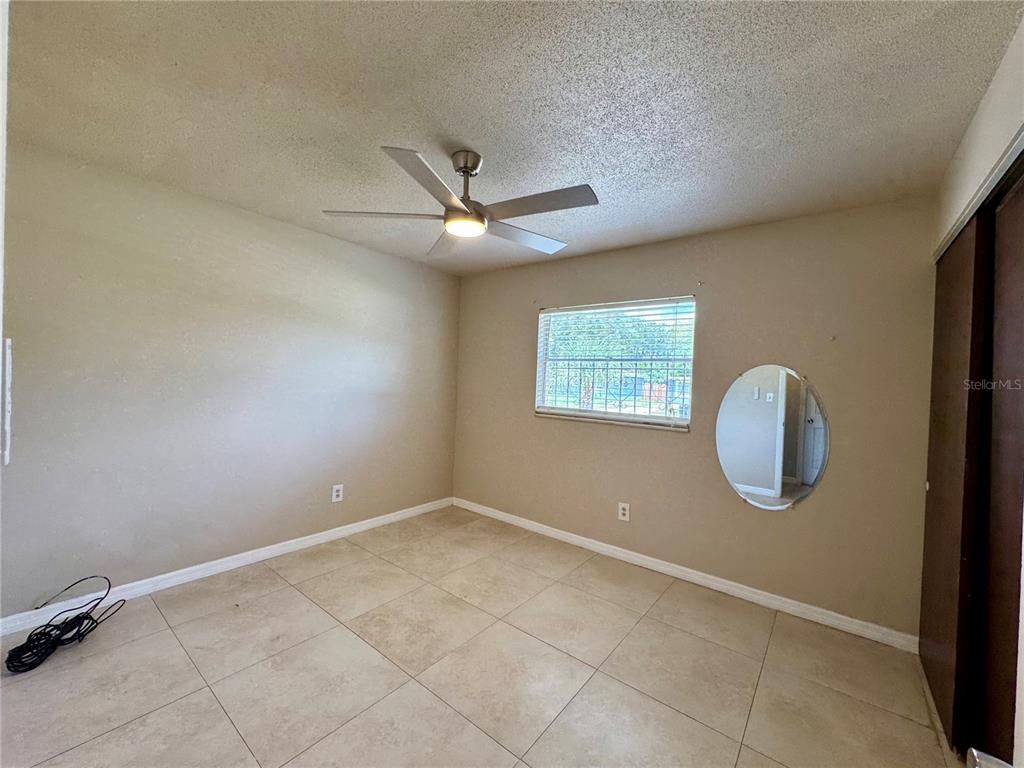 A bedroom with beige walls, tile flooring, a ceiling fan, and a circular wall mirror — 775 HILLVIEW DRIVE, ALTAMONTE SPRINGS, FL