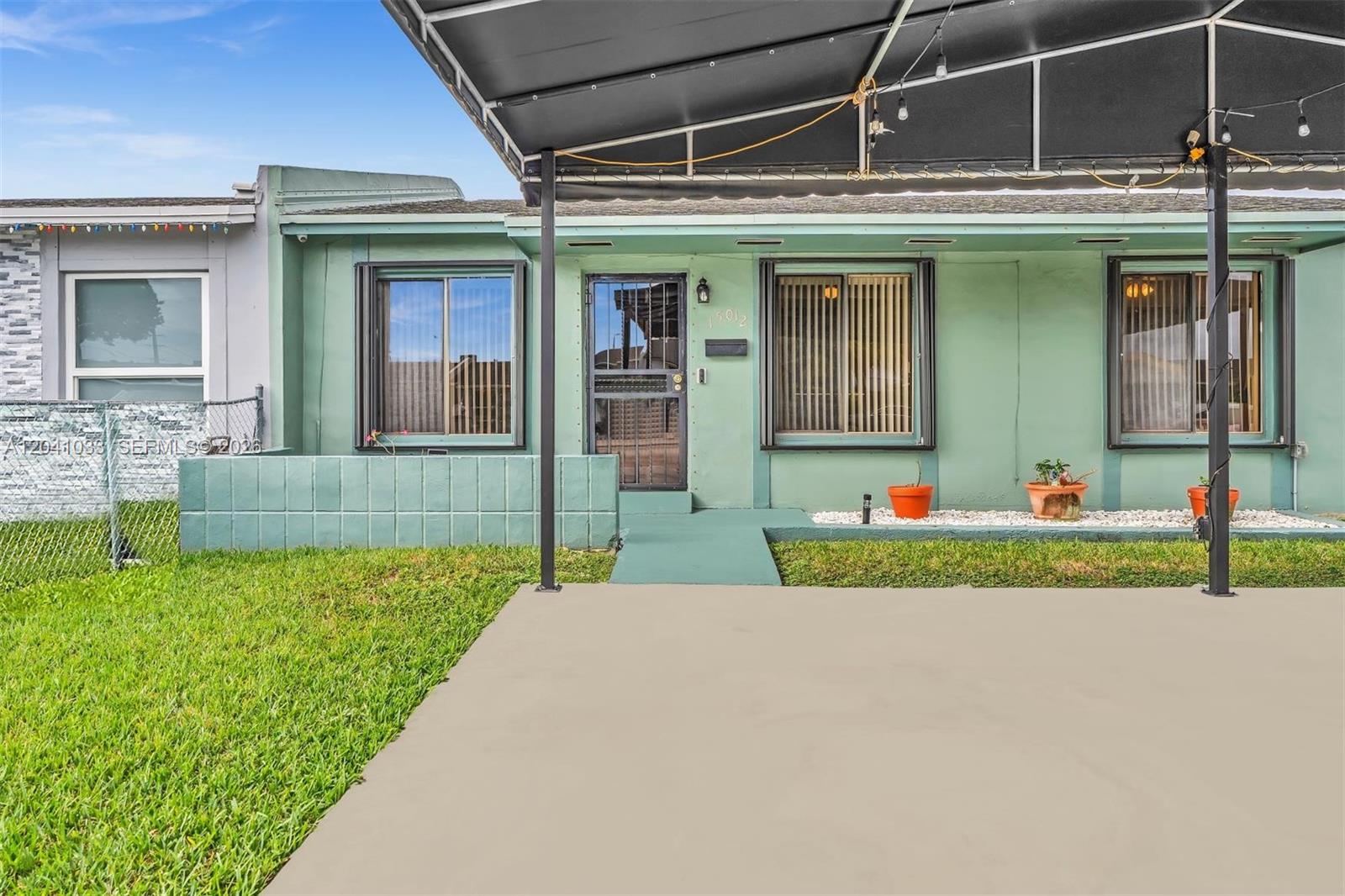 The exterior of a single-story house features green siding, a concrete patio, and a canopy — 15012 SW 113th Ct, Miami FL 33176, MIAMI, FL