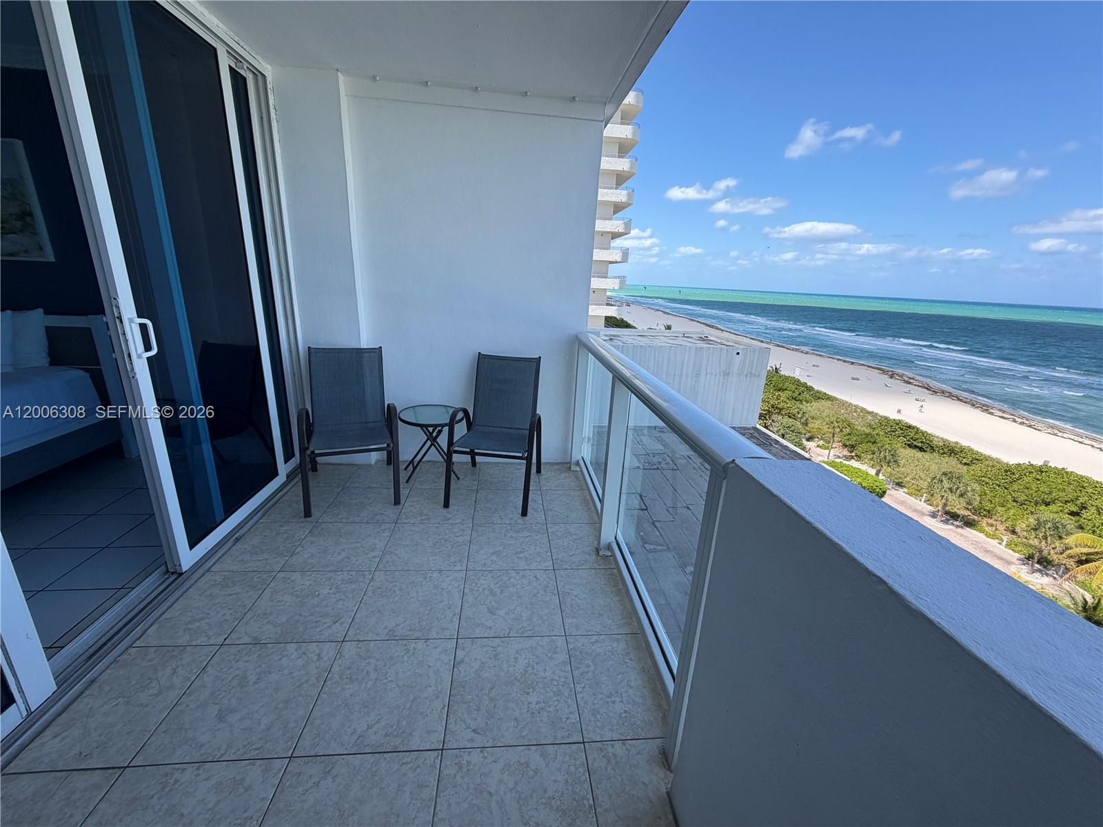A balcony features two chairs, a small table, and a view of the ocean — MIAMI BEACH, FL