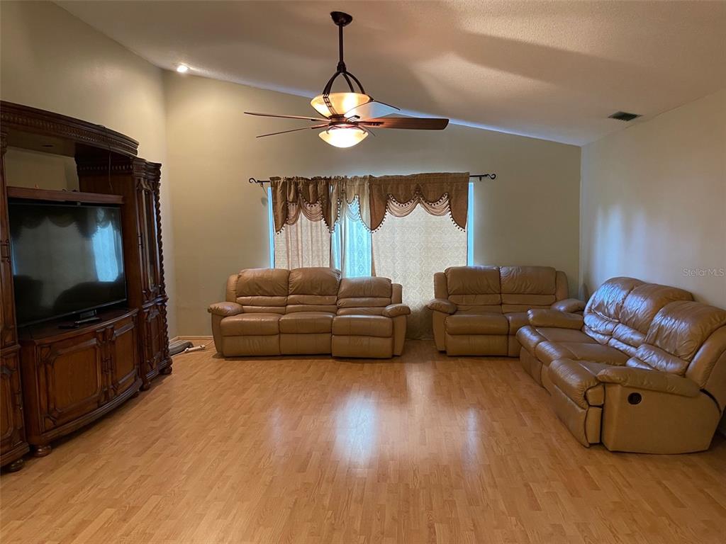 A living room features light wood flooring, tan leather sofas, and a ceiling fan — 6336 WOODEN STREET, NEW PORT RICHEY, FL