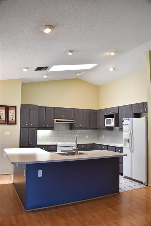 A kitchen features dark cabinets, a blue island with a sink, and a vaulted ceiling — 6336 WOODEN STREET, NEW PORT RICHEY, FL