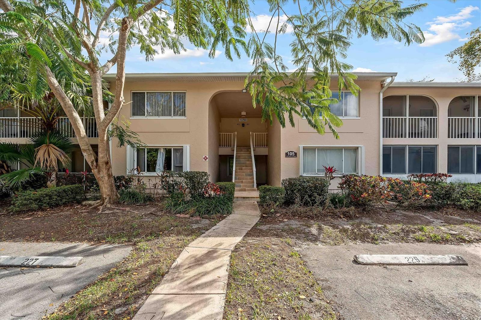 A two-story tan apartment building features a central staircase and a concrete walkway — 13790 Oneida Drive # B1, Delray Beach FL 33446, DELRAY BEACH, FL